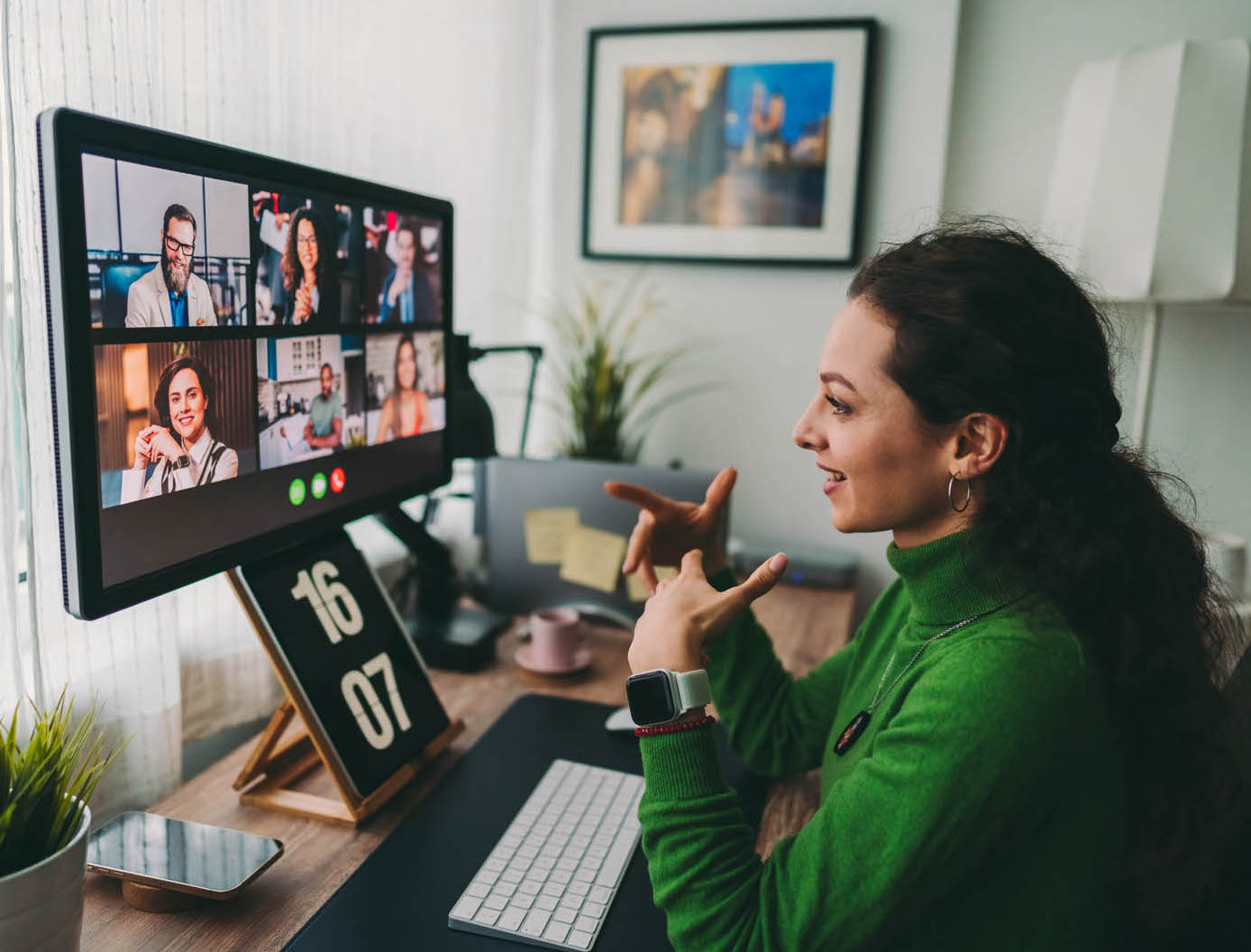 A woman sits at a desk, engaged in a video conference on her computer screen. Image